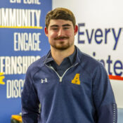 a smiling man in a blue jacket with a yellow letter A on the chest