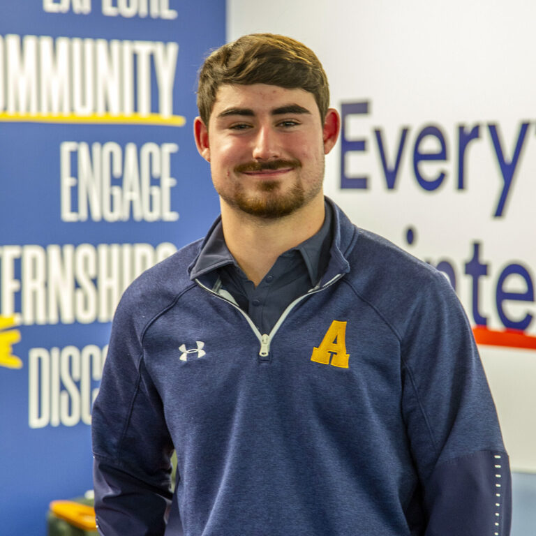 a smiling man in a blue jacket with a yellow letter A on the chest