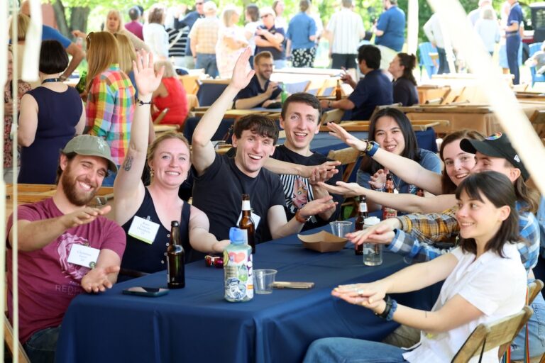 A group of people sit at a table and hold their hands out to resemble Allegheny College gator jaws