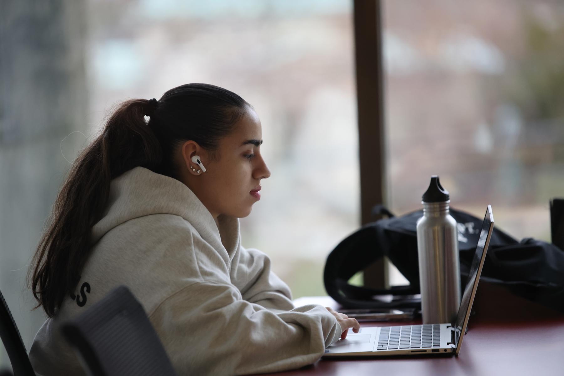 a person sitting at a table using a laptop in front of a window