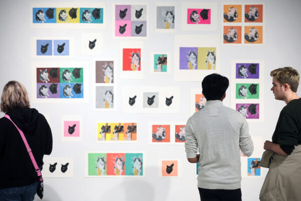 three people view artwork on a wall during an exhibition opening