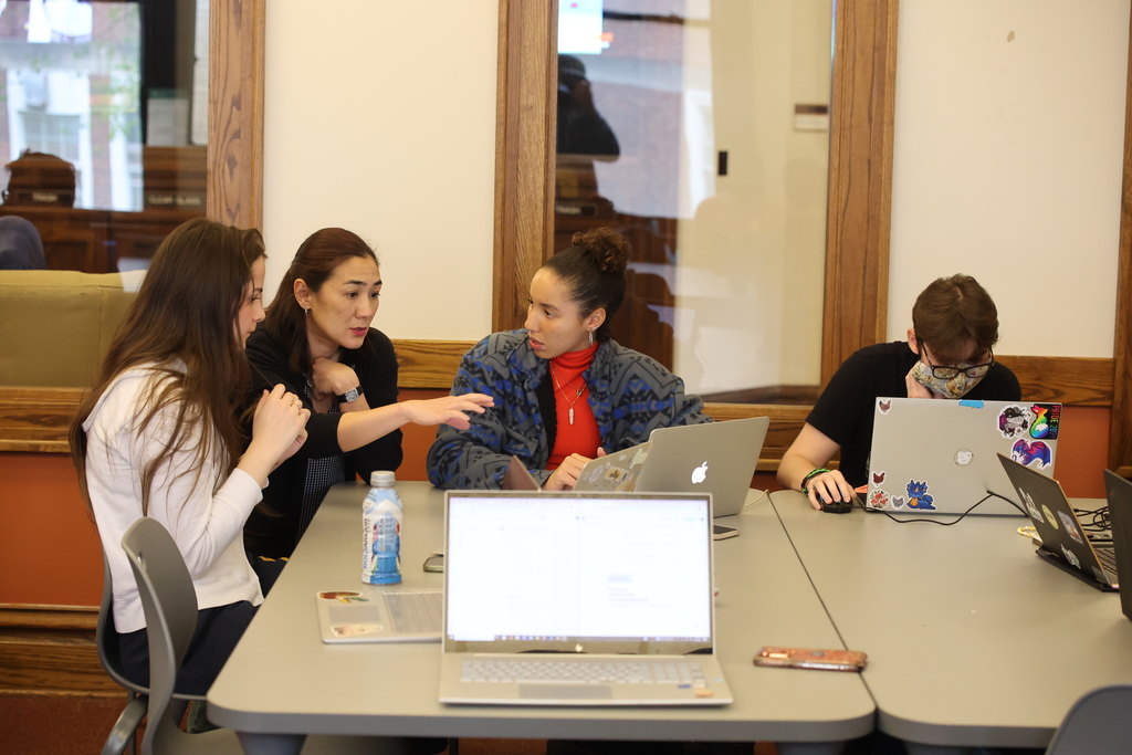 a group of students sitting at a table with laptops talking with each other