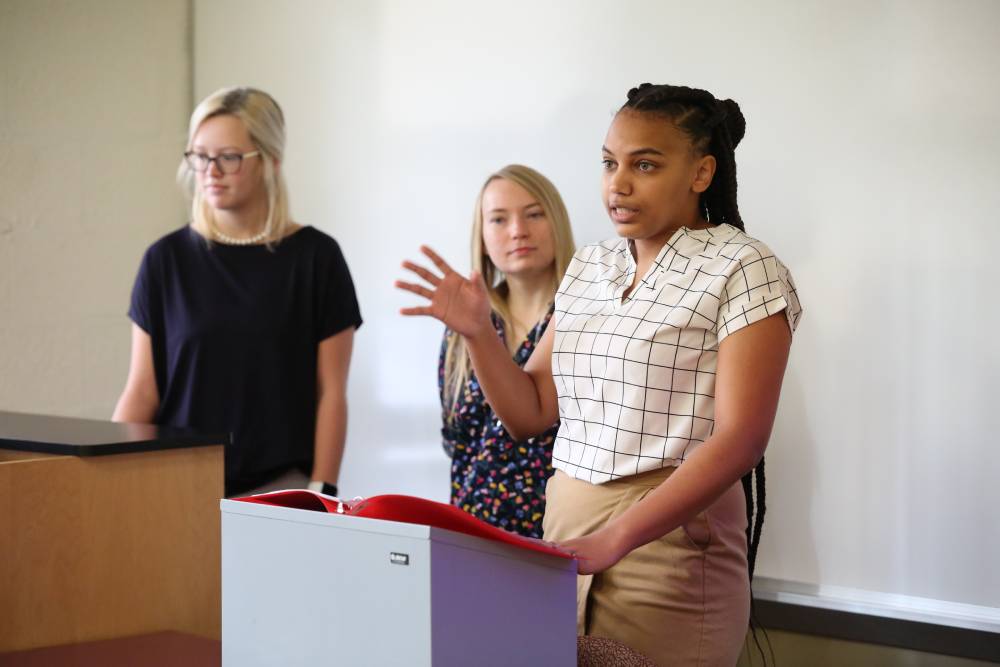 Group of three students presenting at a podium