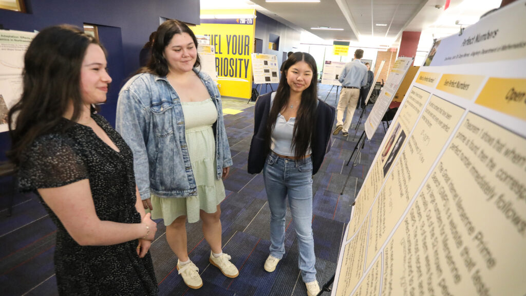 Three students reading a research poster in the library