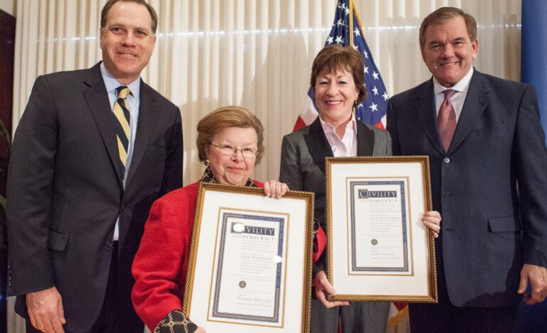 Four people standing with the two in the middle holding framed documents