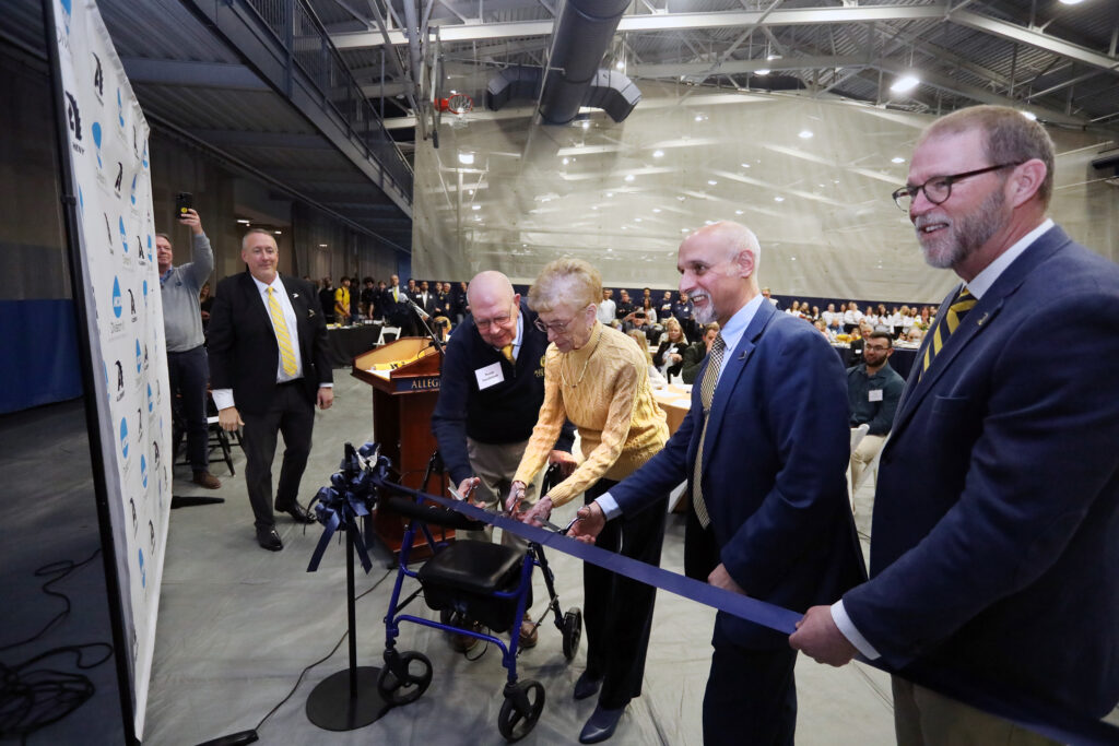 a group of people cutting a blue ribbon with a pair of oversized scissors