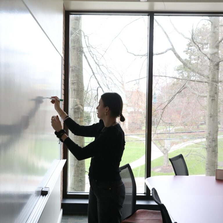 An Allegheny College student writes on a whiteboard in a conference room