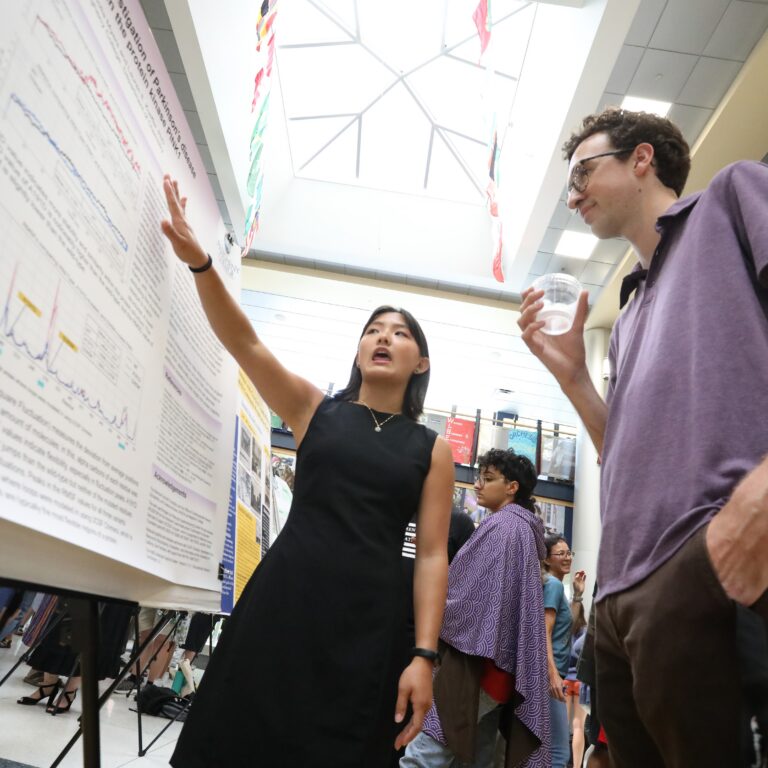 A student presents research board to another student in the Campus Center