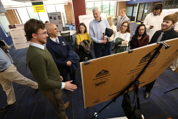 Student presenting their poster to a group of people