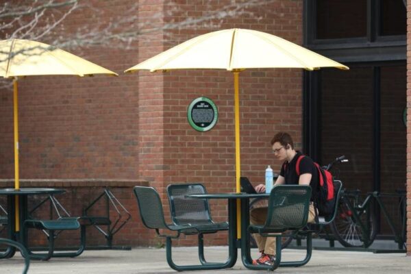 a person sitting at a picnic table under an umbrella