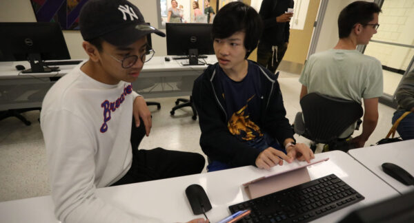 a group of students sitting at a desk looking at a computer