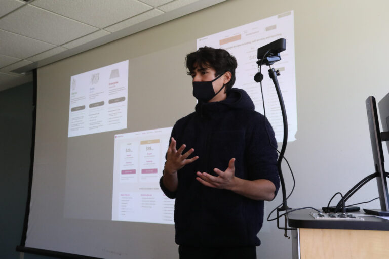 a person wearing a mask speaking in front of a projector screen