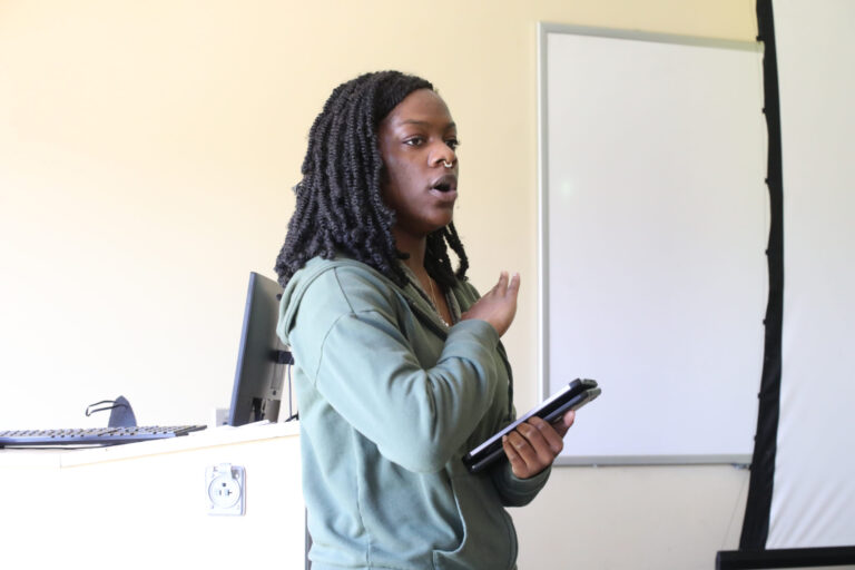 a person woman holding a tablet and speaking in front of a whiteboard