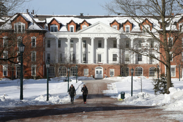 snowy view of a walkway with two people and a white columned building in the background