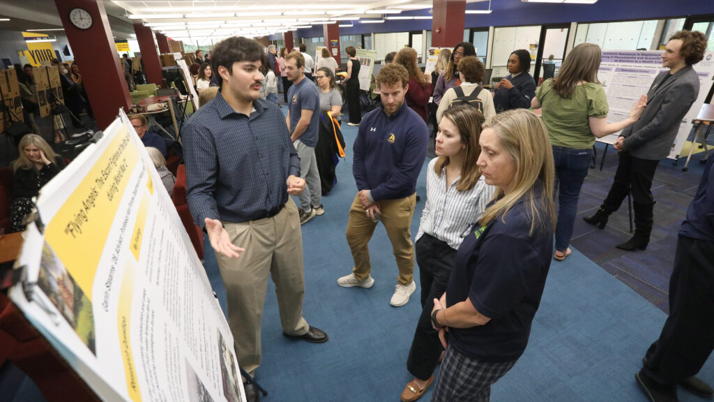 Student speaking about their research to three people