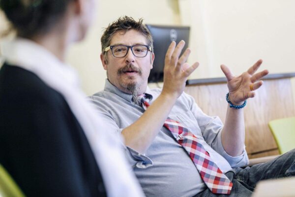 a person in a tie and glasses talking to another person