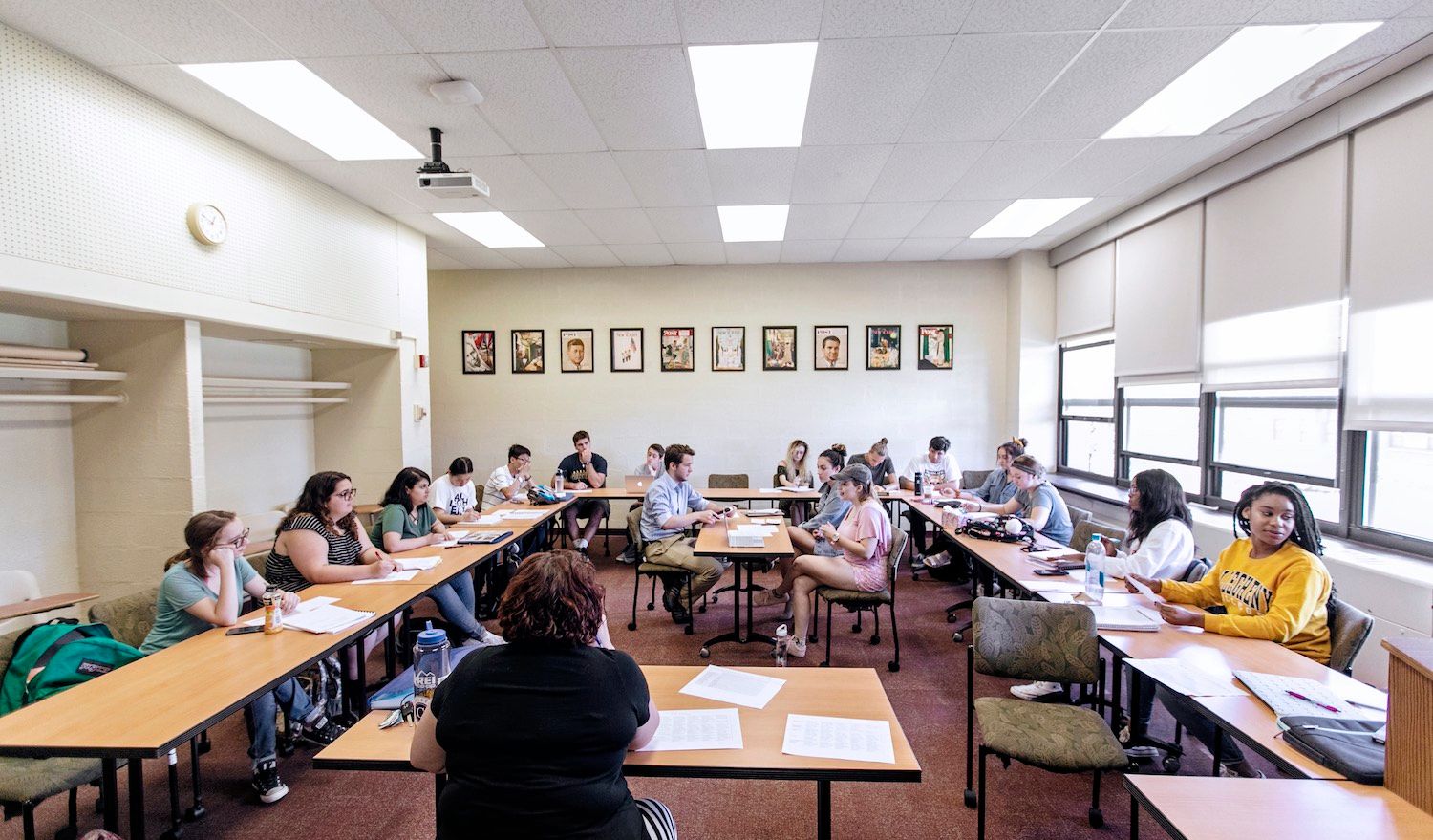 a group of students sitting at tables in a classroom with pictures on the walls behind them