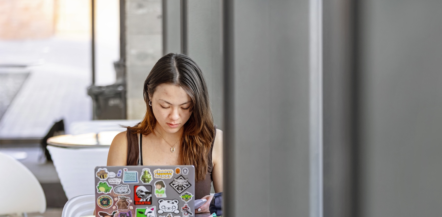 A college students sits in front of their laptop covered in stickers