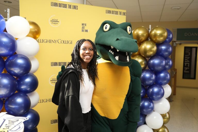 An admitted college student stands next to Allegheny College's mascot Chompers