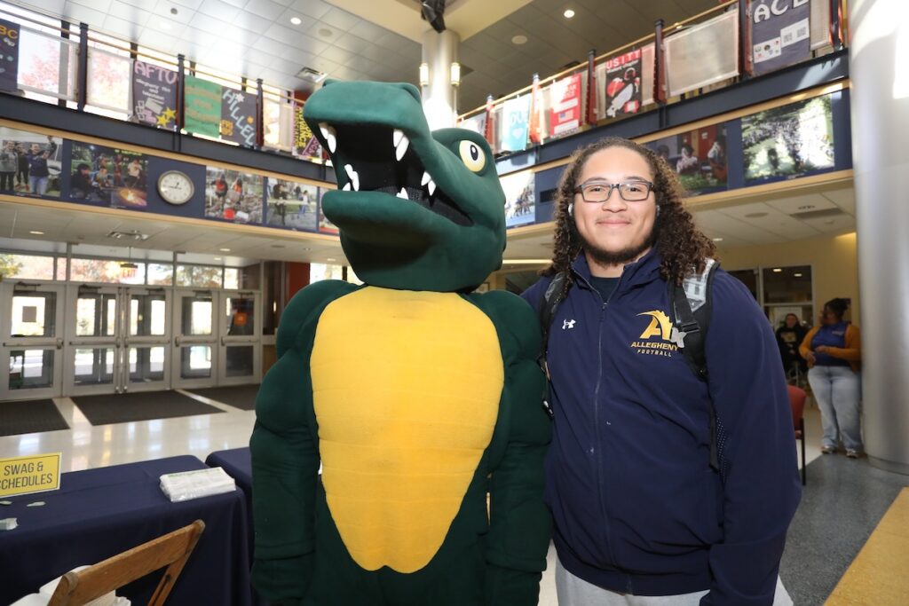 An admitted college students stands with Allegheny College's gator mascot Chompers