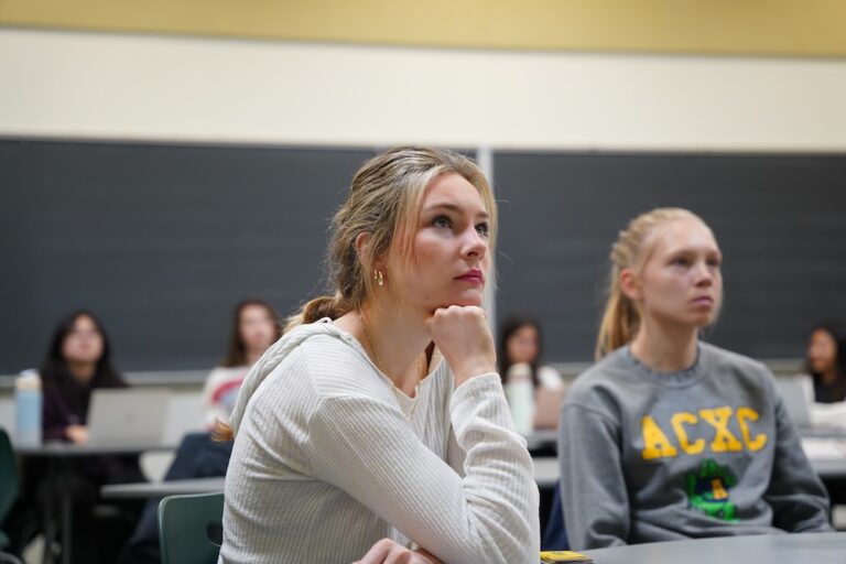 An Allegheny College student sits in a classroom with other students, looking at a board