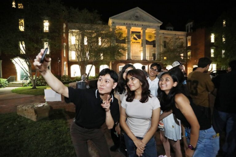 A group of Allegheny College students take a selfie outside of Brooks Hall during a nighttime campus event