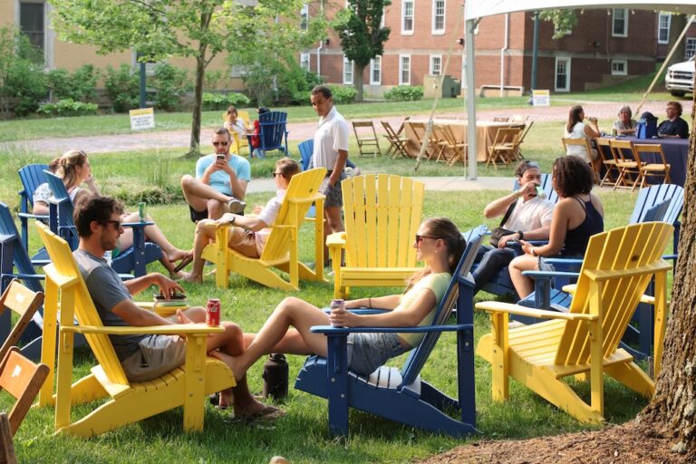 A group of people sit on blue and yellow adirondack chairs
