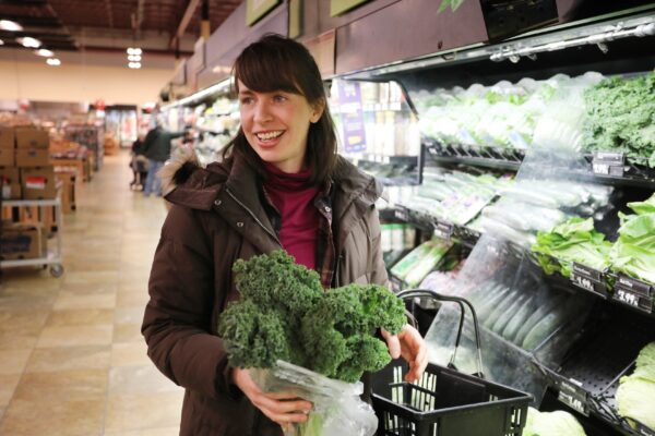 a woman holding a bag of broccoli in a grocery store