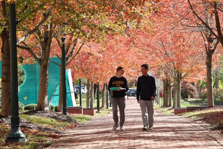 Two Allegheny College students walk down a red brick path lined with trees with red and orange leaves