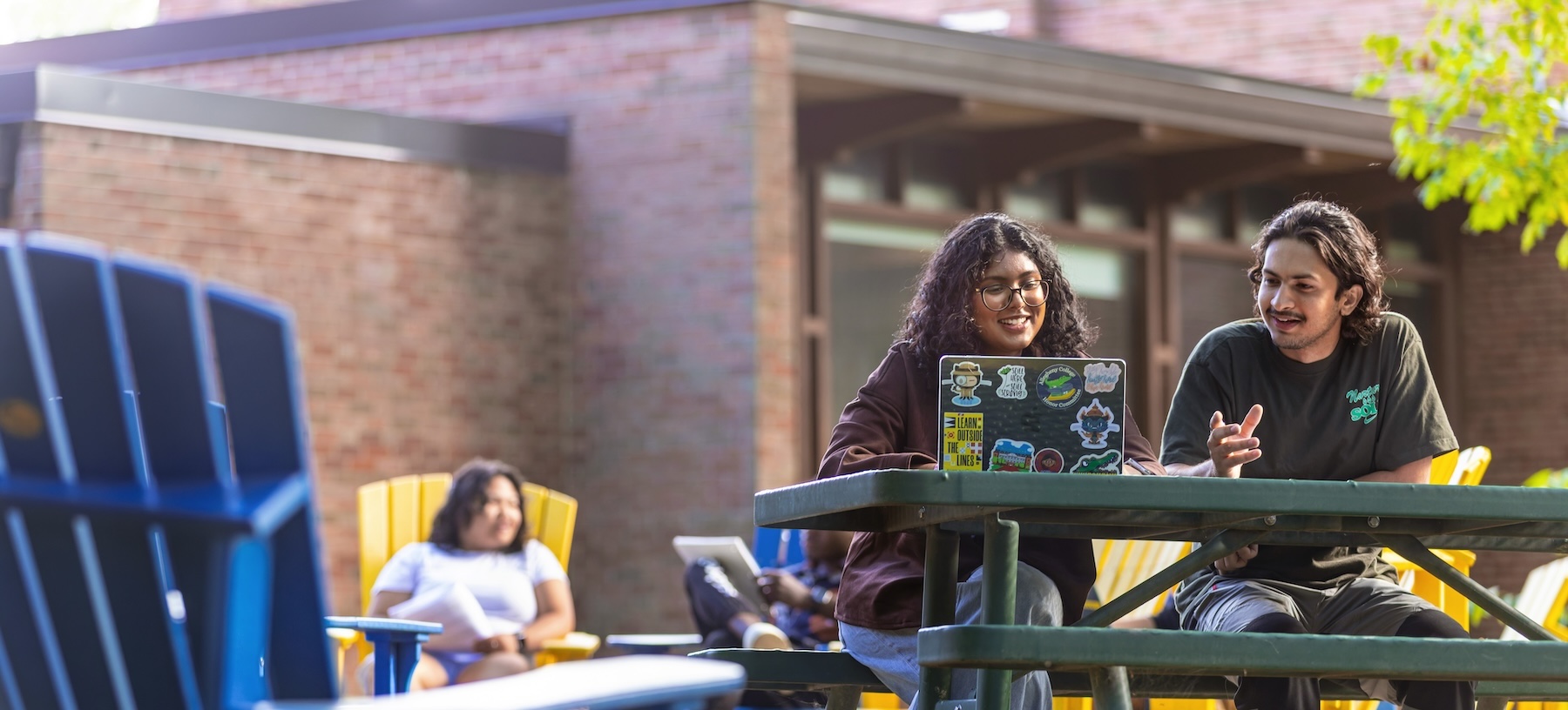 Two Allegheny College students sit at a bench looking at a laptop