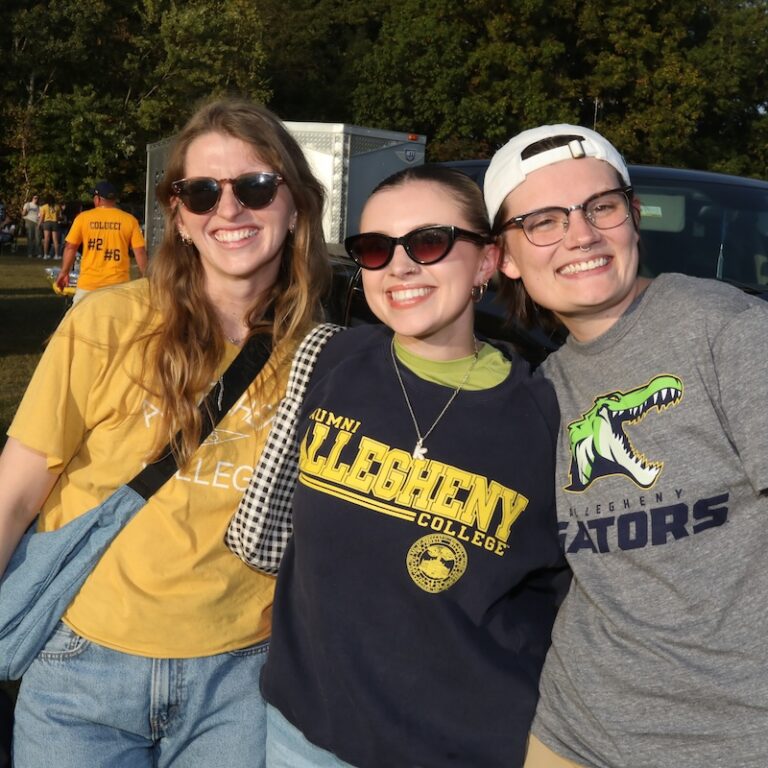 Three Allegheny College students smile at the Blue & Gold Weekend tailgate