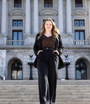 a woman standing on stairs in front of a building with her hands in her pockets