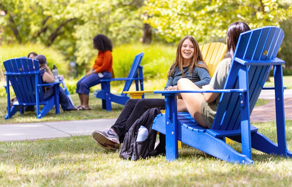 Allegheny College students sit in blue and yellow adirondack chairs
