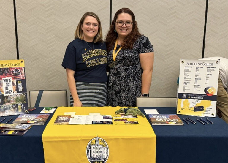 Two women standing at a table that is displaying college collateral materials