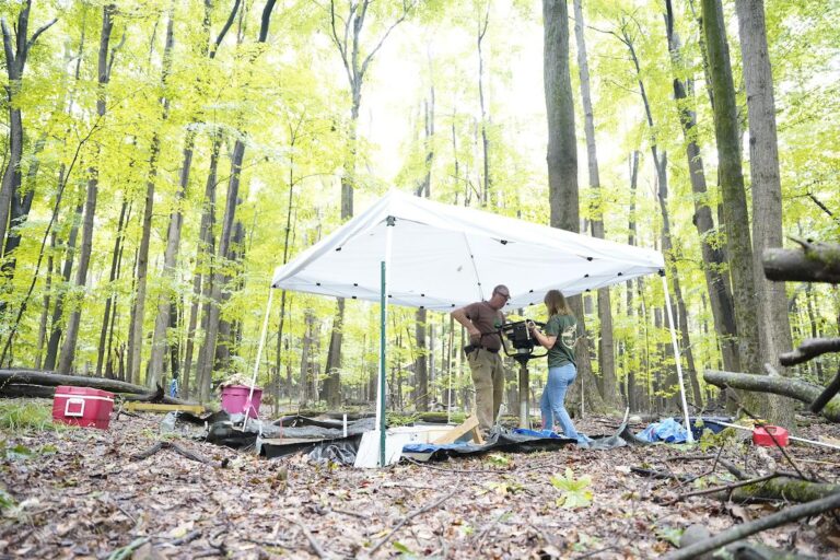 Two people dig into soil with an auger in a forest