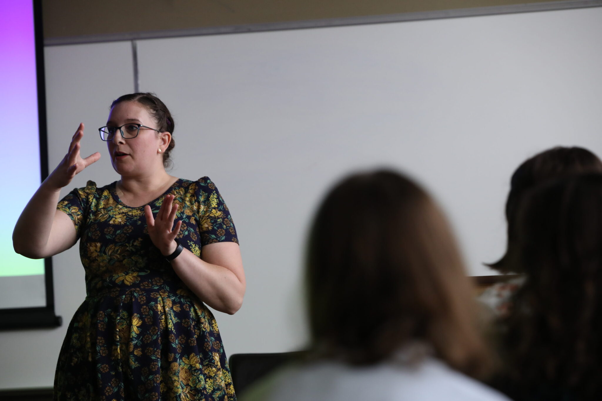 a person in a dress standing in front of a white board while students look on