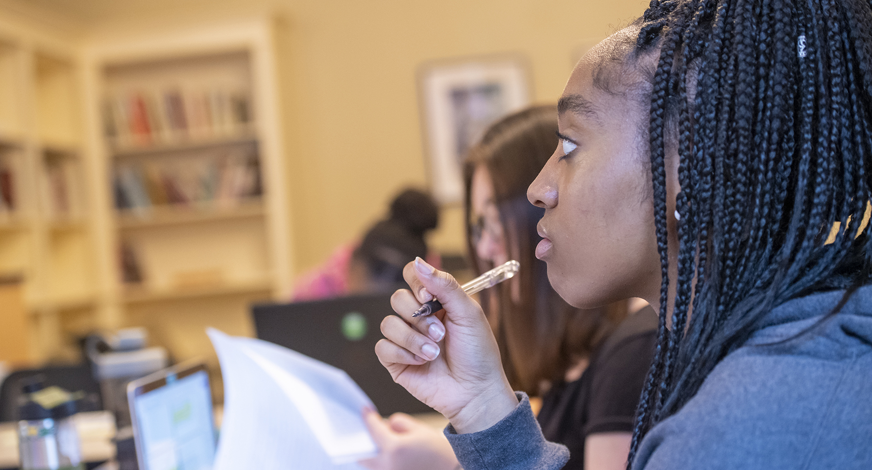 a student holding a pen and looking intently to her left