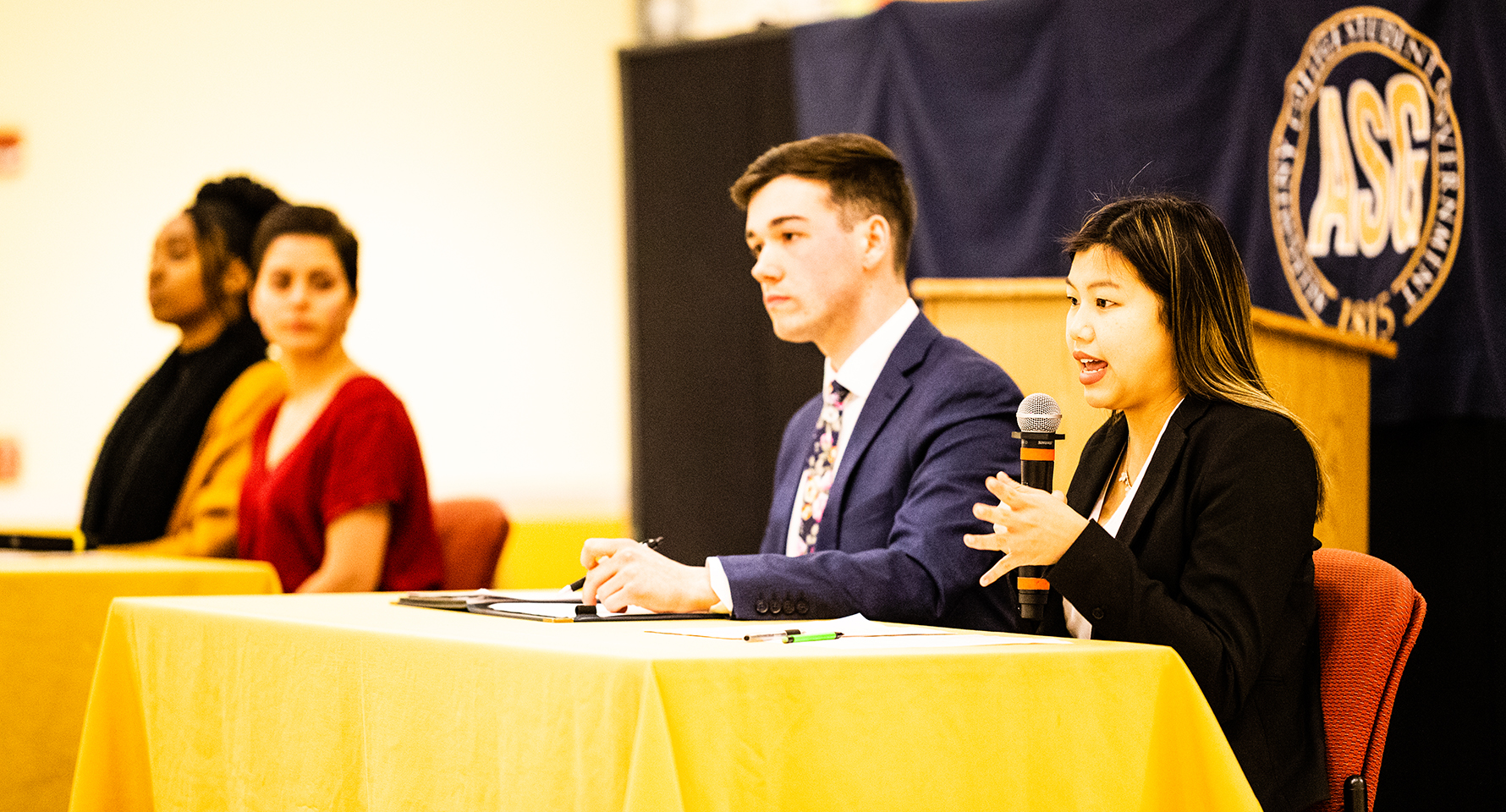 people in formal dress sitting at a table with microphones