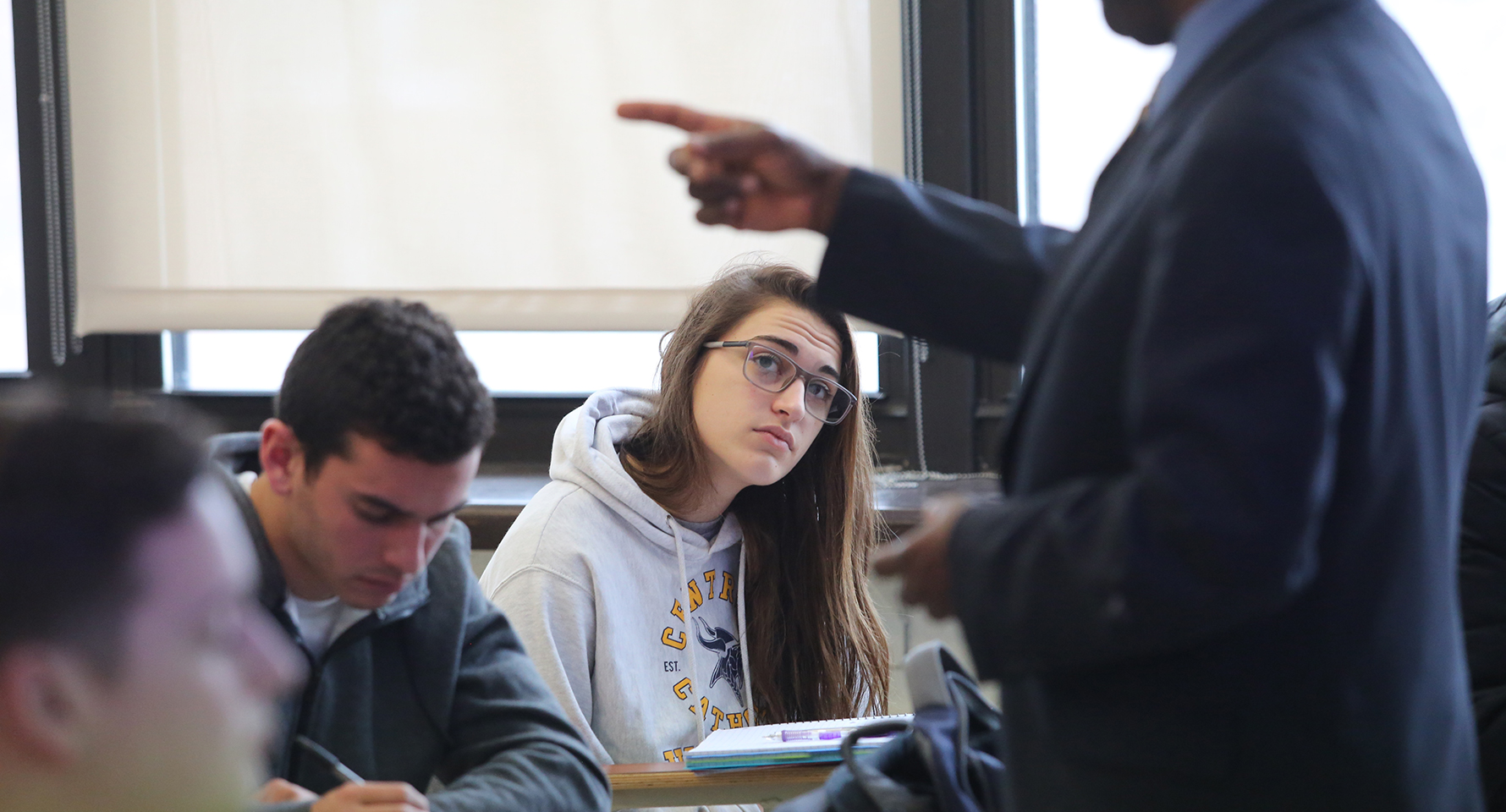 a student sitting at a desk with a professor in front of her