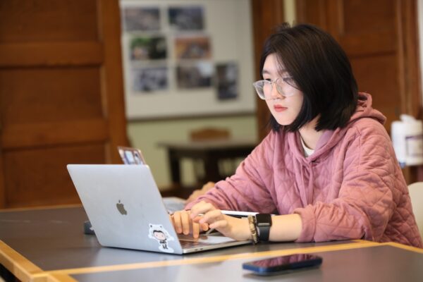 An Allegheny College student works on a silver laptop