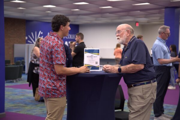 Two people stand at a small roundtable and have a conversation