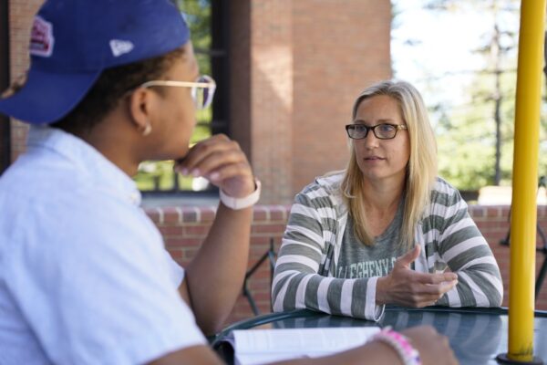 An Allegheny College staff member talks with a student sitting at a round table on a patio
