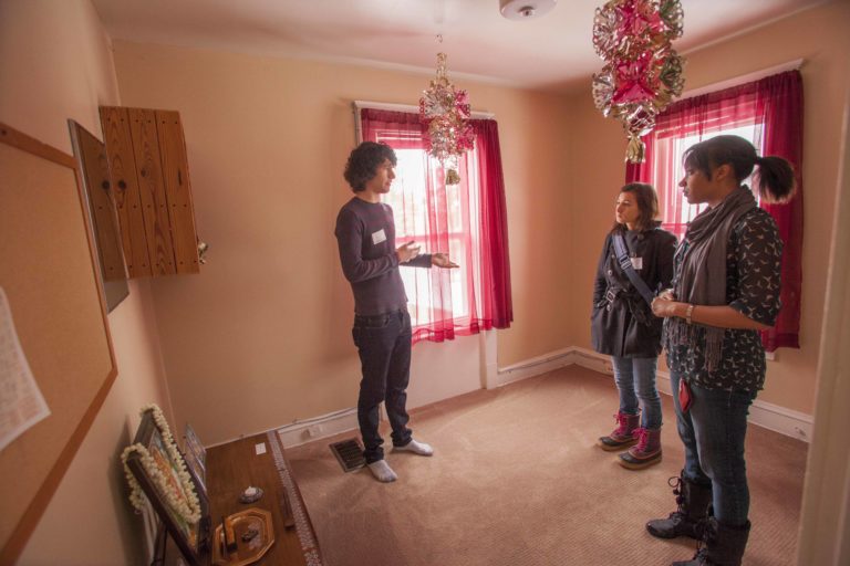 a student talking to two other students in a room with sheer red curtains