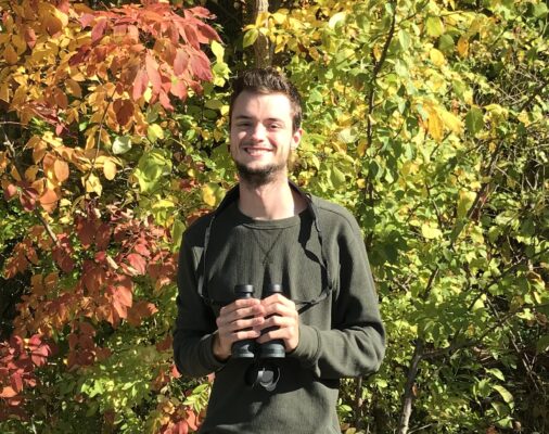 a person holding binoculars in front of trees