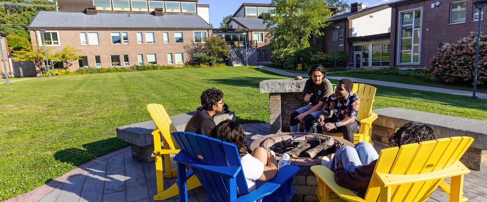 Allegheny College students sit around a bonfire pit in yellow and blue adirondack chairs