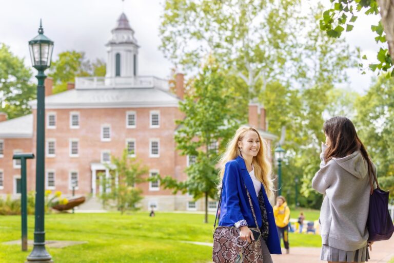 Two Allegheny College students stand on a sidewalk and chat while Bentley Hall is in the background