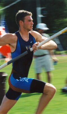 a student athlete in a blue and black tank top holding a pole