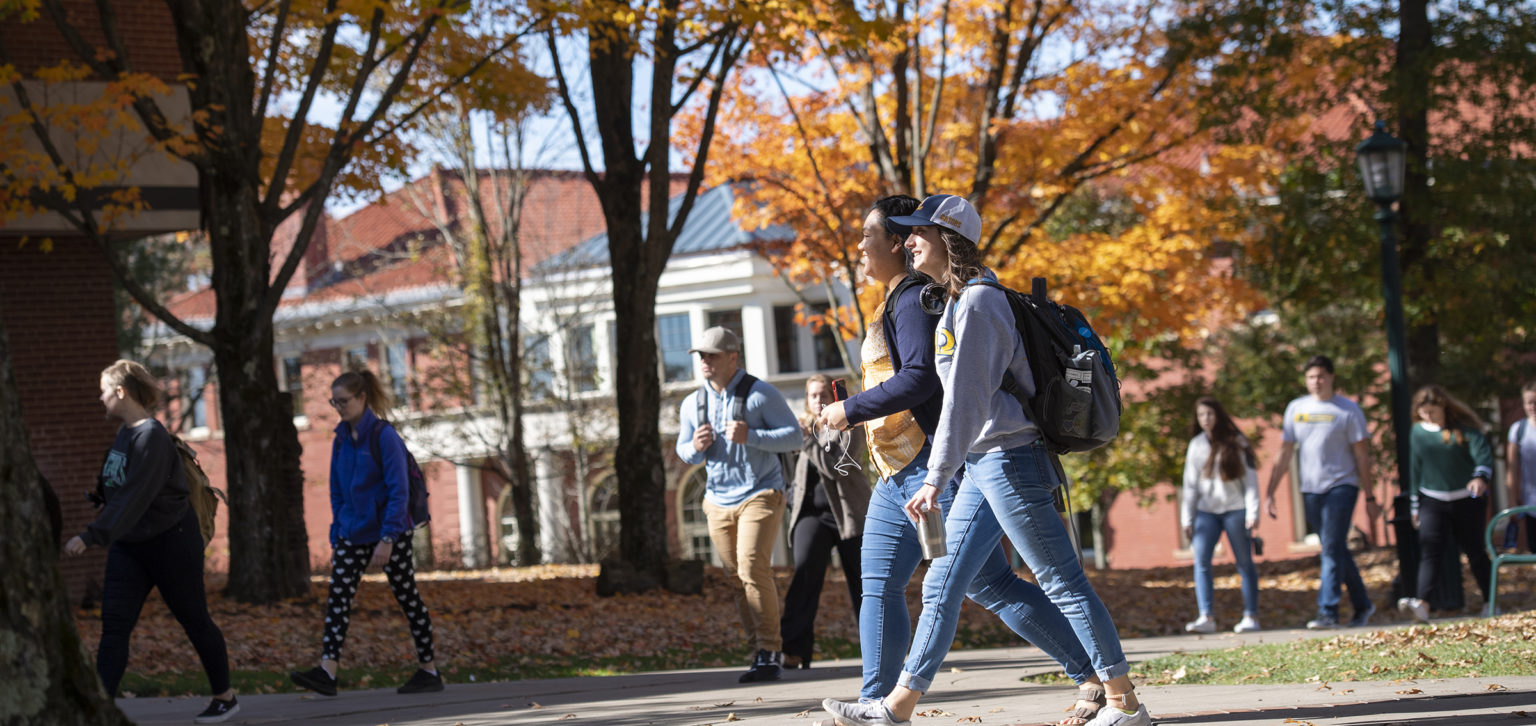 Students walk in front of autumn foliage on campus