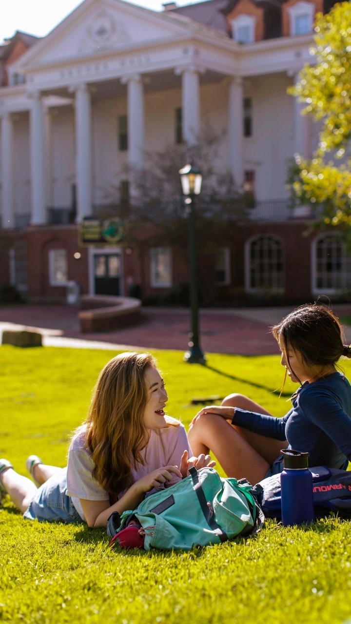 Two people lay on the grass with Allegheny College's Brooks Hall in the background