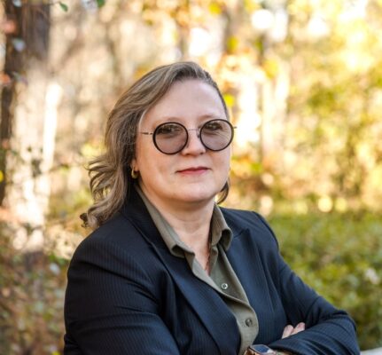 a woman wearing sunglasses and a black jacket posing outdoors